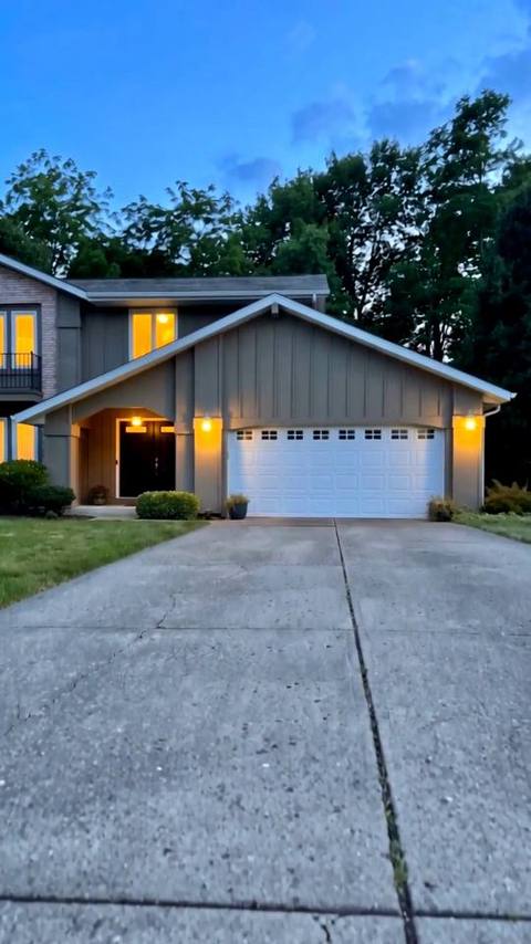 Vertical frame from the reel: the same house at dusk from the driveway, warm light in the windows, no cars